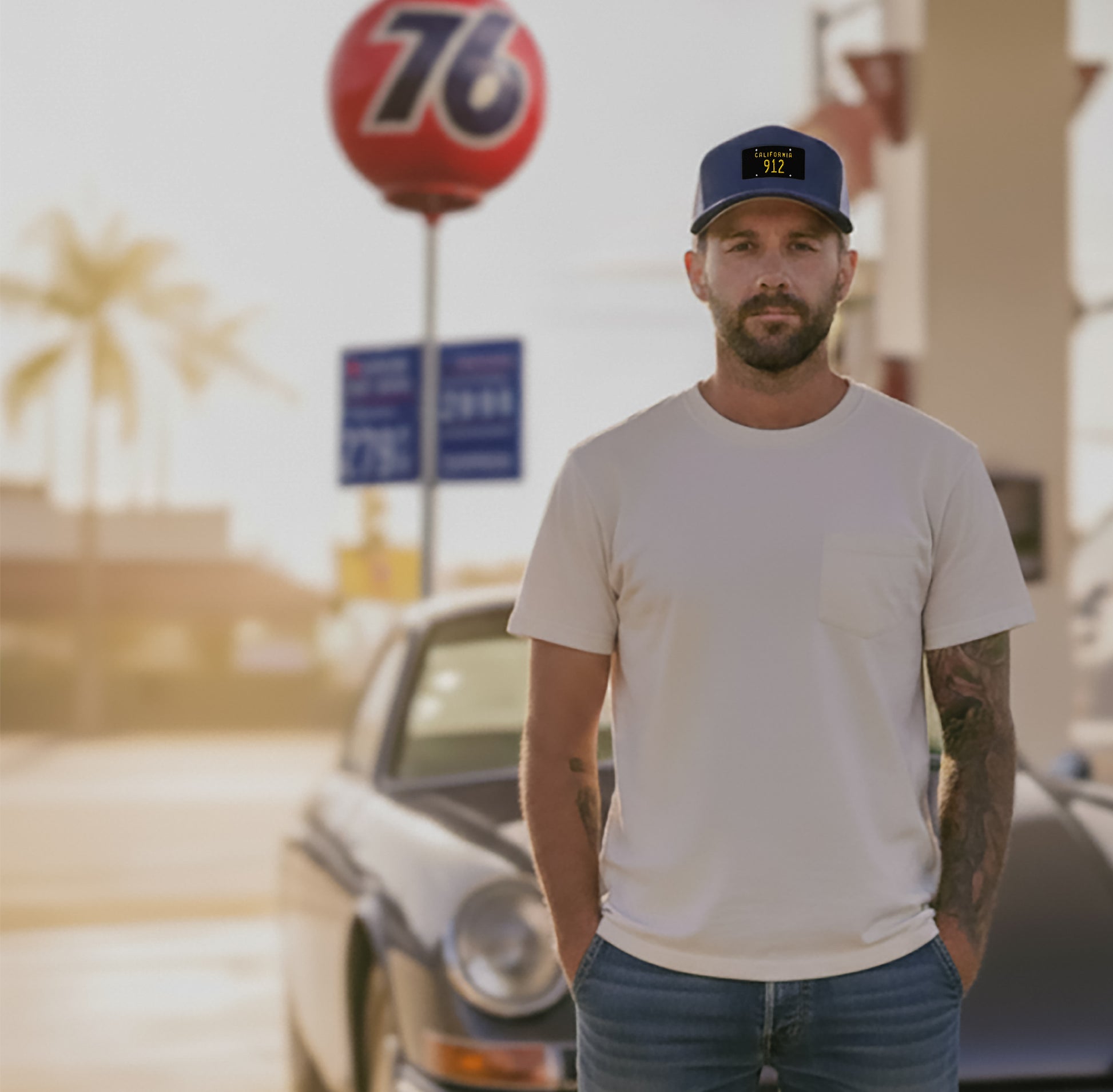 Man standing in front of a classic Porsche at a Union 76 gas station, wearing a Blue Porsche 912 Trucker hat