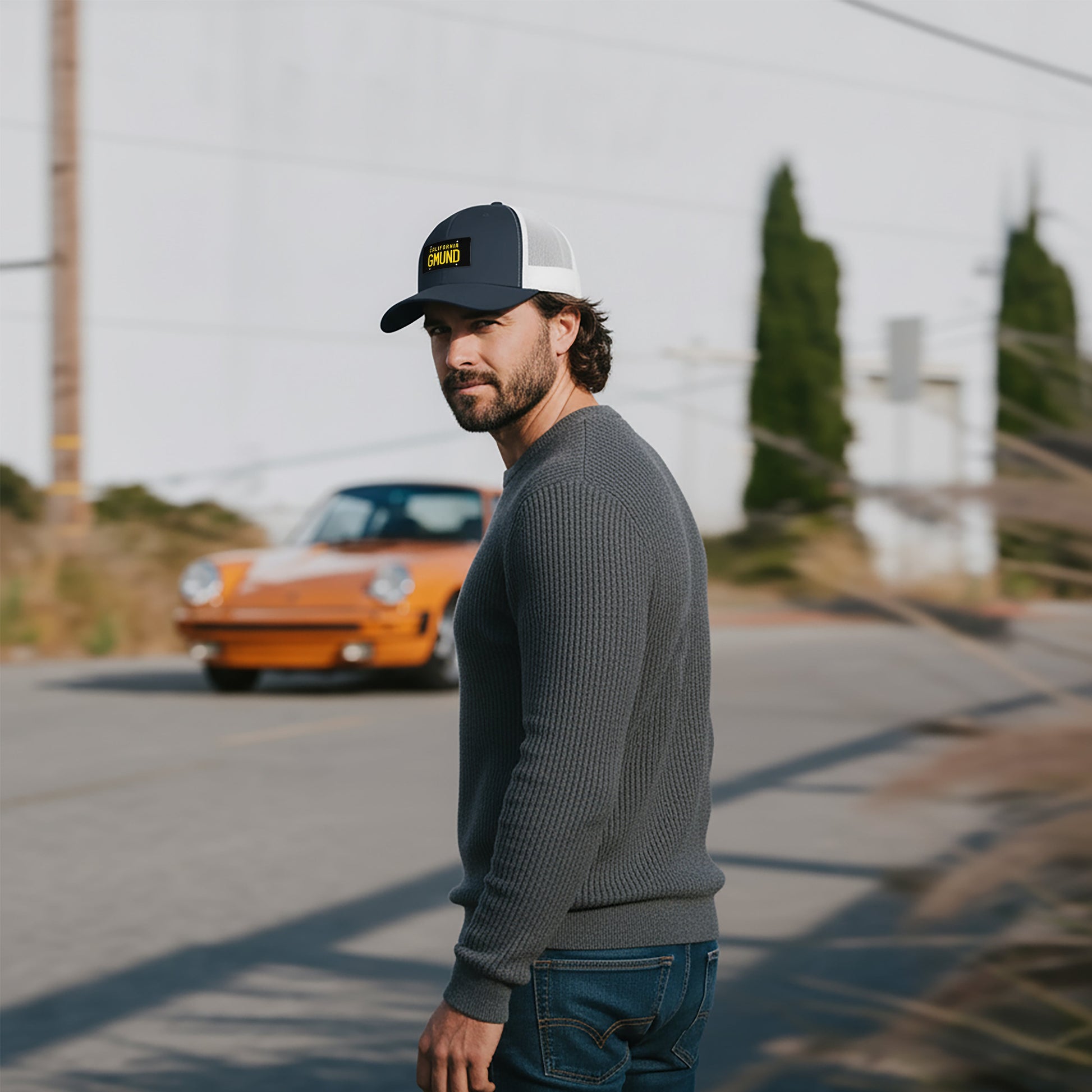 Man wearing a Navy/White Porsche GMUND Trucker hat, standing in front of a vintage Porsche 911.