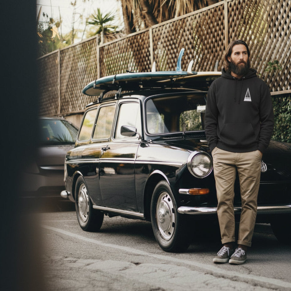 Man stands in front of a VW Squareback wearing a vintage style Harbour Surfboards hoodie in black.