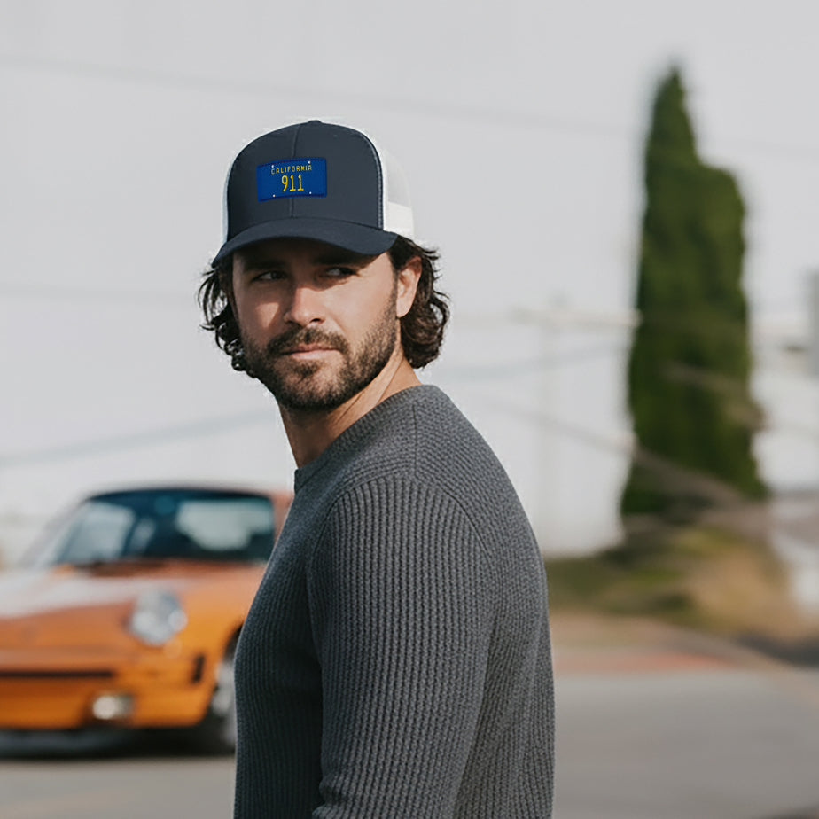Man wearing a California 911 Trucker Hat, standing in front of an orange Porsche 911.