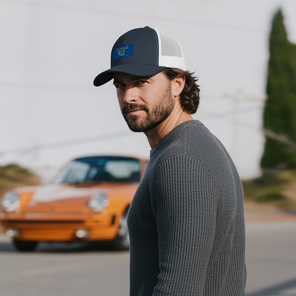 Man wearing a Porsche 912 cap with an orange 911 in the background