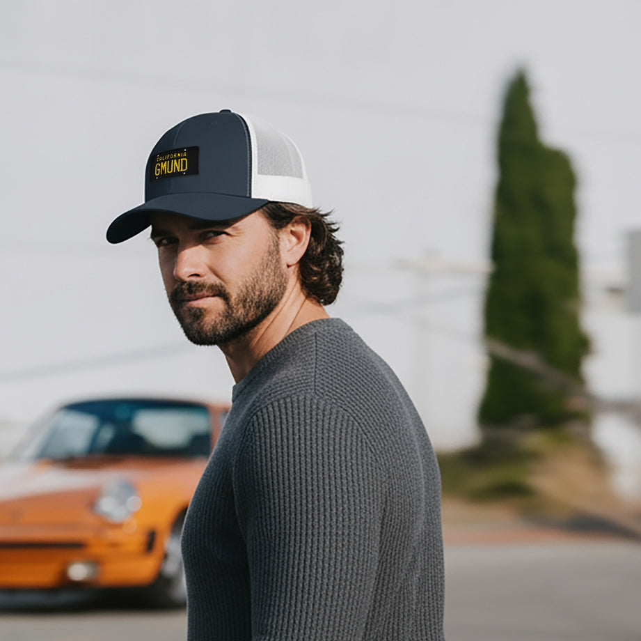 Man wearing a Navy/White Porsche GMUND Trucker hat, standing in front of a vintage Porsche 911.