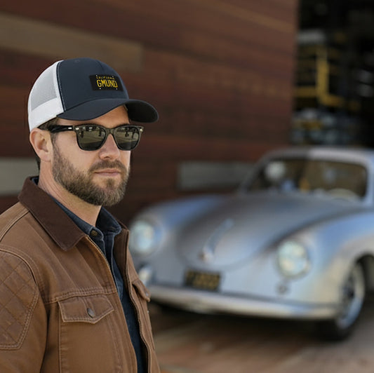 Man wearing a Navy/White Porsche GMUND Trucker hat and sunglasses standing in front of a vintage Porsche 356 Pre A.