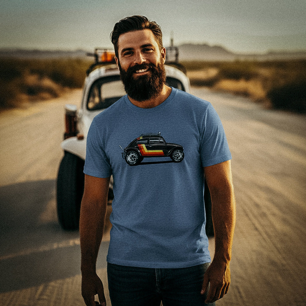 Man standing in a desert with a vintage Baja bug in the background, wearing a 'Stripes' Baja Bug T-shirt.