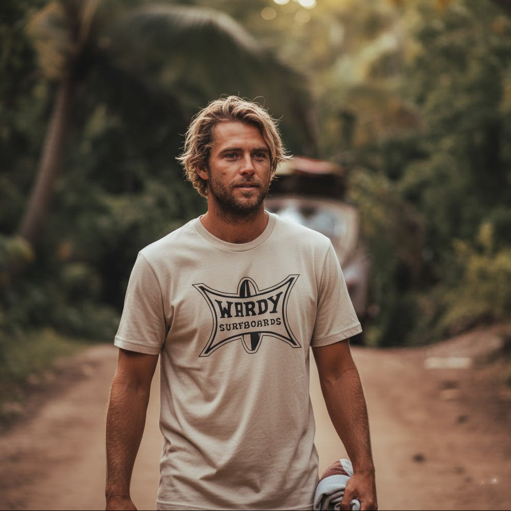 Man stands in front of a VW Bug with surfboards on the roof, wearing a Vintage style Wardy Surfboards T-shirt.