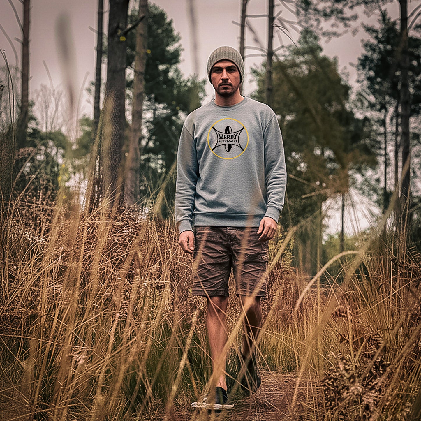 Man wearing a gray Wardy Surfboards sweatshirt in a forest setting.