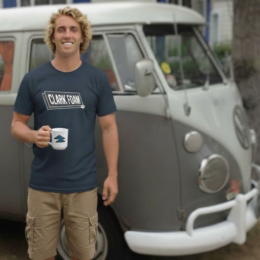 Man stands in front of a VW Split Screen Bus wearing a Vintage style Clark Foam Surf T-shirt.
